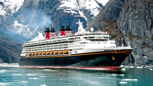 The Disney Wonder ocean liner sailing through water and ice next to a glacier mountain